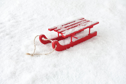 Red wooden sledge with rope in snow covered with snowflakes.