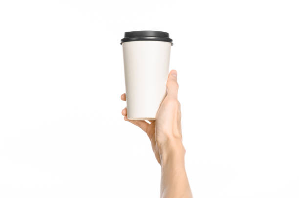 istock Breakfast and coffee theme: man's hand holding white empty paper coffee cup with a brown plastic cap isolated on a white background in the studio, advertising of coffee first-person view 1051319776