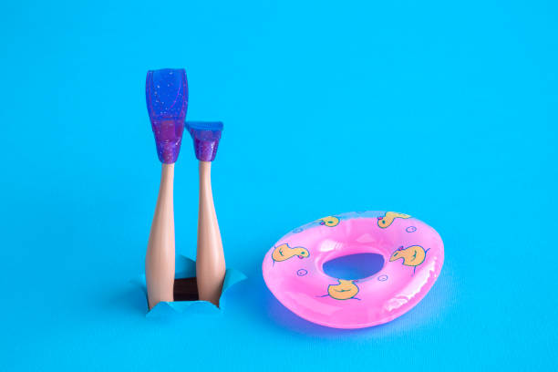 Doll legs with snorkel fins and inflatable pool float on blue sea background minimal creative abstract concept. Close up of inflatable pool float and scuba diver feet with snorkel fins diving. Space for copy. scuba diving photos stock pictures, royalty-free photos & images