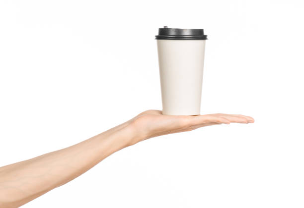 istock Breakfast and coffee theme: man's hand holding white empty paper coffee cup with a brown plastic cap isolated on a white background in the studio, advertising coffee 1051323132