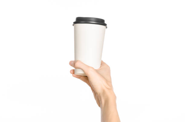istock Breakfast and coffee theme: man's hand holding white empty paper coffee cup with a brown plastic cap isolated on a white background in the studio, advertising of coffee first-person view 1051327816