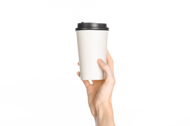 istock Breakfast and coffee theme: man's hand holding white empty paper coffee cup with a brown plastic cap isolated on a white background in the studio, advertising of coffee first-person view 1051328006