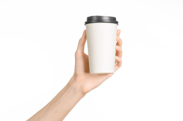 istock Breakfast and coffee theme: man's hand holding white empty paper coffee cup with a brown plastic cap isolated on a white background in the studio, advertising coffee 1051328432
