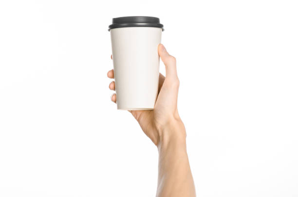 istock Breakfast and coffee theme: man's hand holding white empty paper coffee cup with a brown plastic cap isolated on a white background in the studio, advertising of coffee first-person view 1051328462