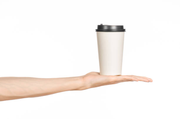 istock Breakfast and coffee theme: man's hand holding white empty paper coffee cup with a brown plastic cap isolated on a white background in the studio, advertising coffee 1051331594