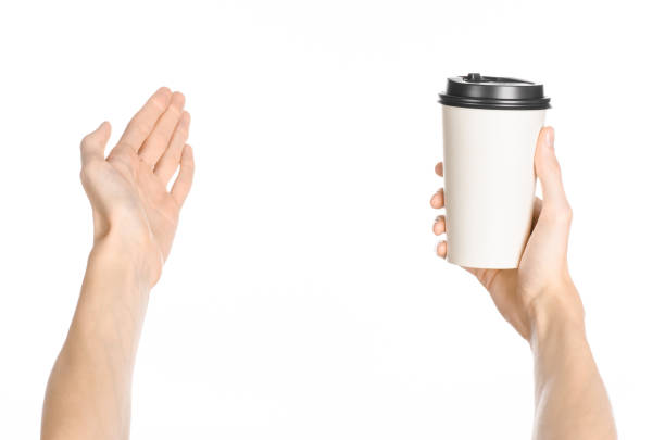 istock Breakfast and coffee theme: man's hand holding white empty paper coffee cup with a brown plastic cap isolated on a white background in the studio, advertising of coffee first-person view 1051331684