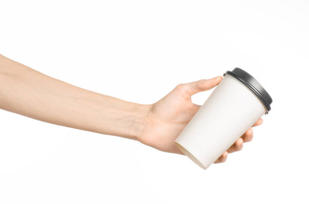 istock Breakfast and coffee theme: man's hand holding white empty paper coffee cup with a brown plastic cap isolated on a white background in the studio, advertising coffee 1051332072