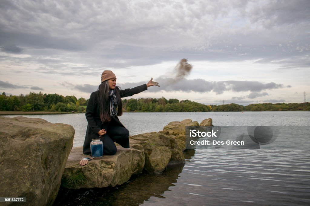 Sad Female Scattering The Cremated Ashes Of A Loved One From A Funeral Urn A Sad Asian Woman Scattering The Cremated Ashes Of A Loved One From A Funeral Urn Cremation Stock Photo