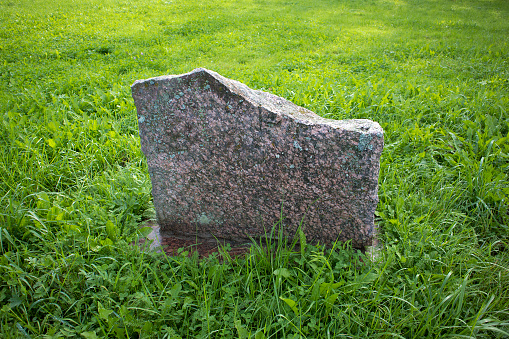Flat memorial blank granite stone in the middle of green juicy grass field
