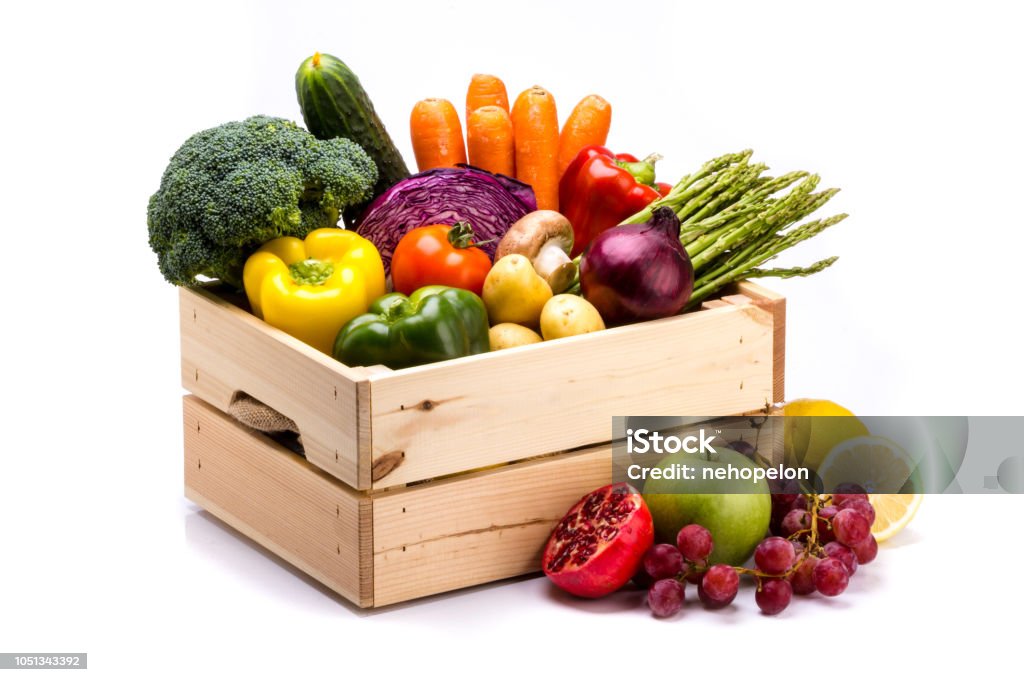 Pine box full of colorful fresh vegetables and fruits on a white background Pine box full of colorful fresh vegetables and fruits on a white background, ideal for a balanced diet, contains broccoli, cucumber, onion, asparagus, peppers, carrots, apple, grape, lima and potatoes Vegetable Stock Photo