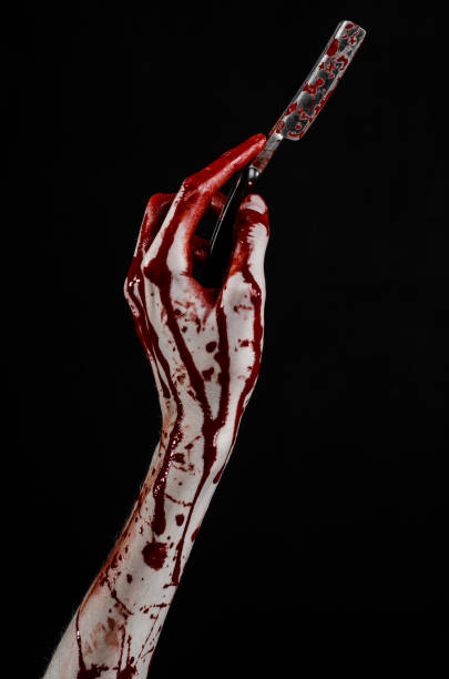 istock Bloody Halloween theme: bloody hand holds a razor sharp old with a dangerous edge isolated on black background 1051343584