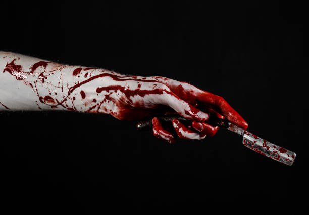 istock Bloody Halloween theme: bloody hand holds a razor sharp old with a dangerous edge isolated on black background 1051345698