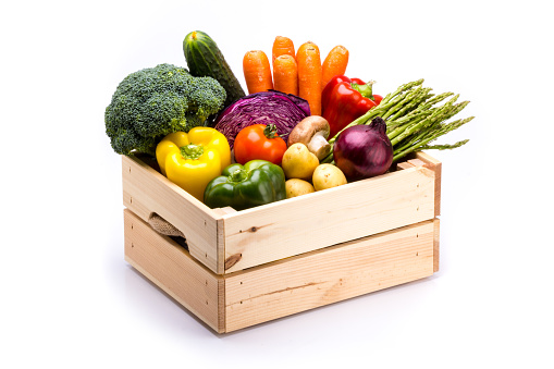Pine box full of colorful fresh vegetables on a white background, ideal for a balanced diet, contains broccoli, cucumber, onion, asparagus, peppers, carrots, and potatoes