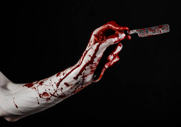 istock Bloody Halloween theme: bloody hand holds a razor sharp old with a dangerous edge isolated on black background 1051346432