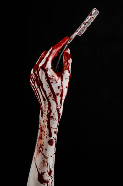 istock Bloody Halloween theme: bloody hand holds a razor sharp old with a dangerous edge isolated on black background 1051346702