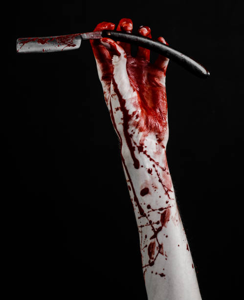 istock Bloody Halloween theme: bloody hand holds a razor sharp old with a dangerous edge isolated on black background 1051346988