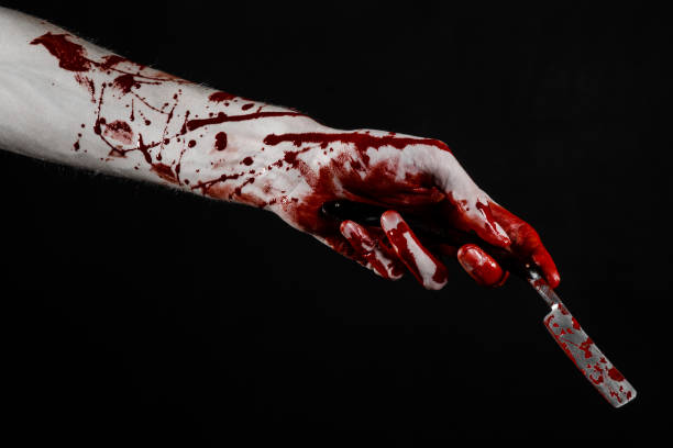 istock Bloody Halloween theme: bloody hand holds a razor sharp old with a dangerous edge isolated on black background 1051348264