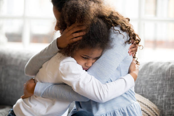 Black mother and daughter embracing sitting on couch Black African mother embrace little preschool frustrated kid sitting on couch together at home. American loving mother supports disappointed daughter sympathizing, making peace after scolding concept sulking stock pictures, royalty-free photos & images