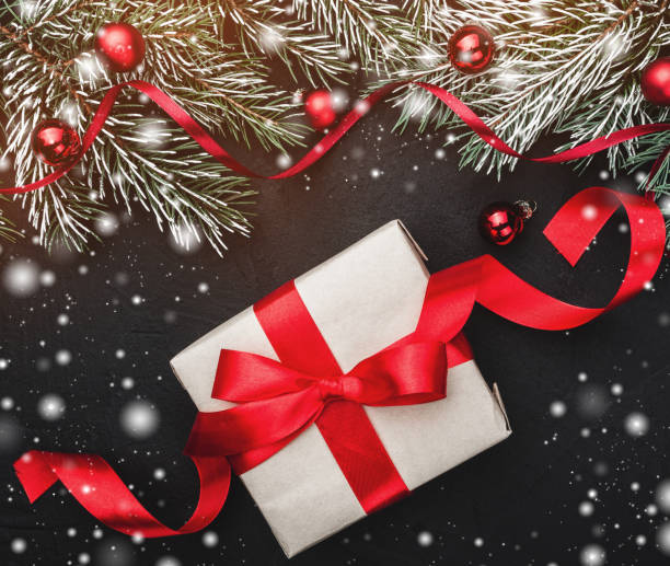 istock Winter card. A red slack gift on a black stone background. With fir branches adorned with red balls. Top view. Effect of lights and snow 1051386782