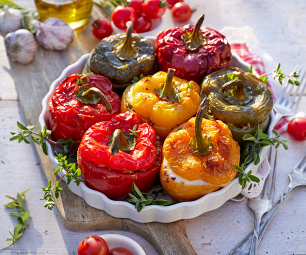 pimentão assado com cogumelos, arroz, queijo e ervas preenchendo uma assadeira sobre uma mesa de madeira branca. - stuffed stuffed pepper pepper bell pepper - fotografias e filmes do acervo