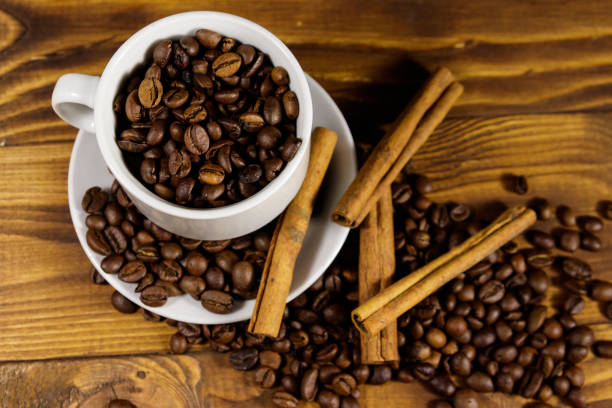istock Coffee beans in white cup and cinnamon sticks on wooden table. Top view 1051397474