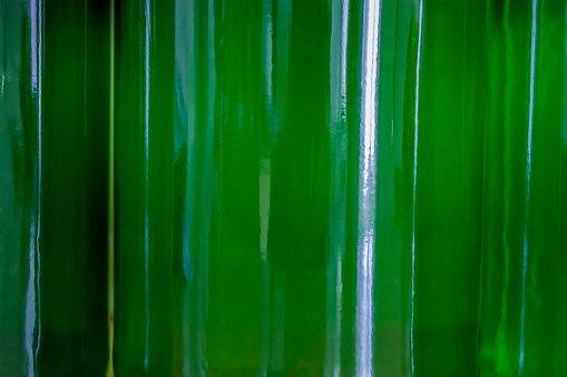 three full transparent green bottles that touch each other, through which the bends light - closeup