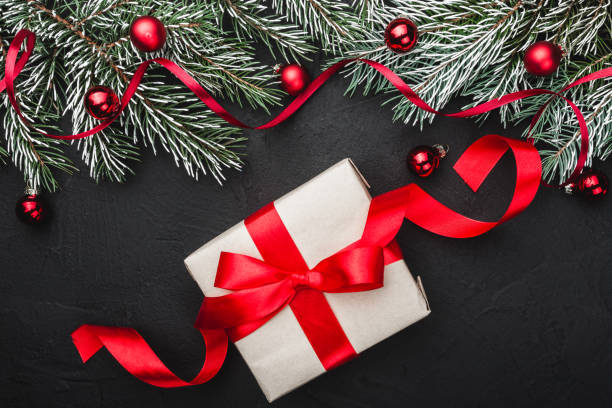 istock Winter card. A red slack gift on a black stone background. With fir branches adorned with red balls. Top view. 1051402744