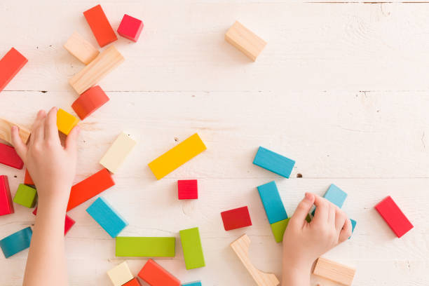 istock Top view on child's hands playing with colorful wooden bricks on the white table background.Kid building with geometric shapes. Learning and education concept. 1051405602