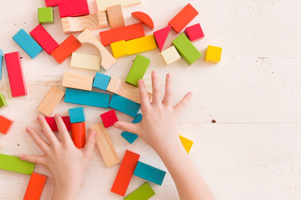 istock Top view on child's hands playing with colorful wooden bricks on the white table background..Kid building with geometric shapes. Learning and education concept. 1051405622