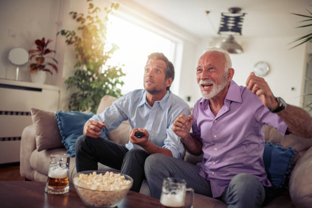 Two men watching football game Two men watching football game,drinking beer and eating popcorn at home. old football stock pictures, royalty-free photos & images