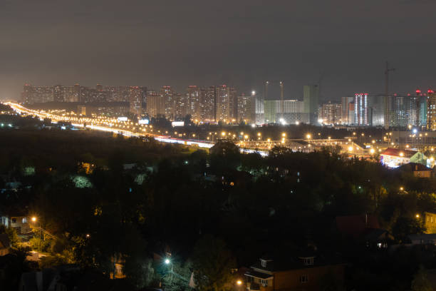 istock Evening city lights are lit from the windows. Road with a passing vehicle. Construction cranes at night. 1051413988