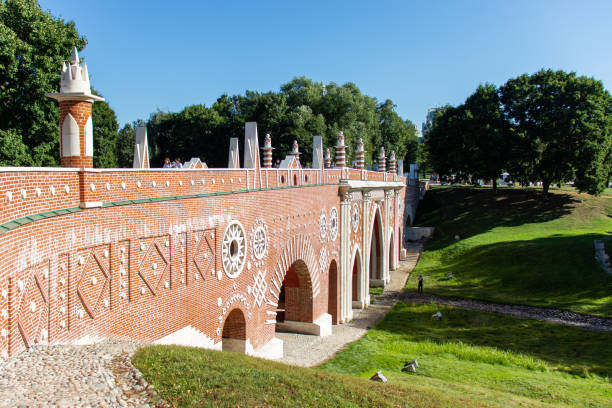 istock Arched bridge of red brick with white elements. Green grass, white stone paths. Green dense trees. 1051414136