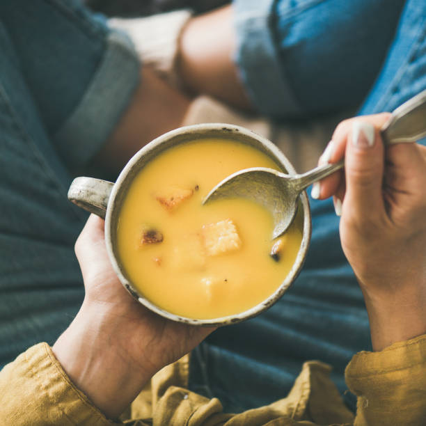 female keeping mug of warming pumpkin cream soup, square crop - smooth part of colors yellow imagens e fotografias de stock