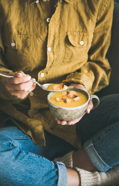 istock Woman sitting and eating pumpkin soup from mug 1051438432