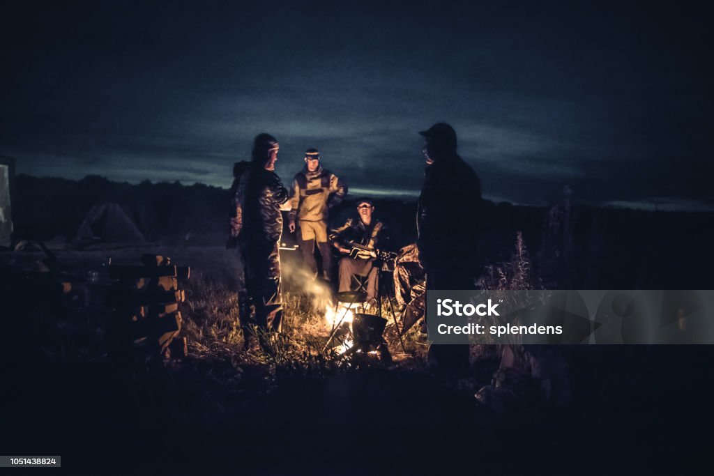 Groupe de touristes de voyageurs de gens hommes feu de camp dans le camp de plein air de repos après une longue journée de chasse dans la nuit - Photo de Chasseur libre de droits