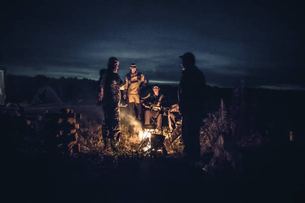 gruppo di uomini viaggiatori turisti riposo campo fuoco in campo all'aperto dopo lunga giornata di caccia nella notte - friendly fire foto e immagini stock