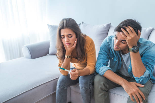 Sad stressed couple with pregnancy test sitting at home Sad stressed couple with pregnancy test sitting at home. Upset woman is looking in pregnancy test. Frustrated man is sitting next to her.  Worried about the serious consequences infertility stock pictures, royalty-free photos & images