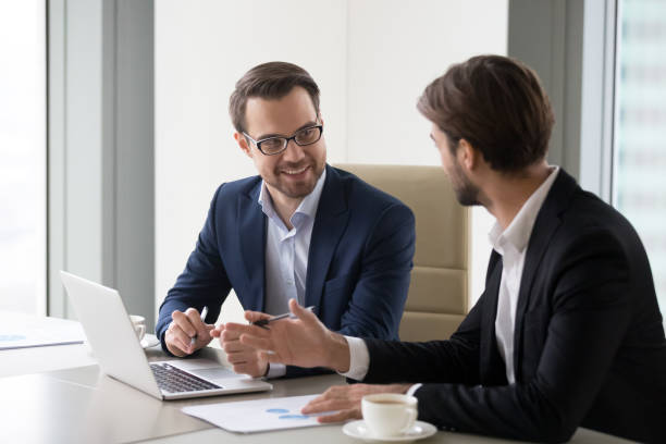 istock Smiling businessmen using laptop discussing business projects 1051453338