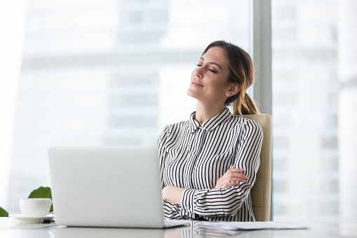 Smiling businesswoman sitting in office chair relaxing with eyes closed, calm female worker or woman ceo feeling peaceful resting at workplace dreaming about positive things distracted from work