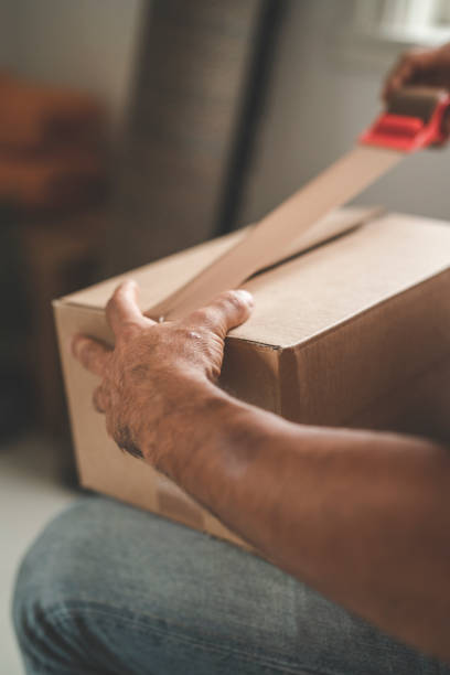 A mature hispanic man is packing and unpacking as he is moving into a new house. Taping up cardboard boxes.