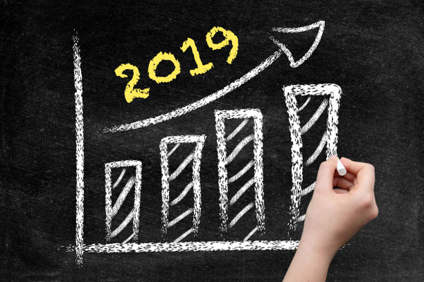 istock Year 2019, ascending arrow and bar graph on blackboard with woman hand 1051457044