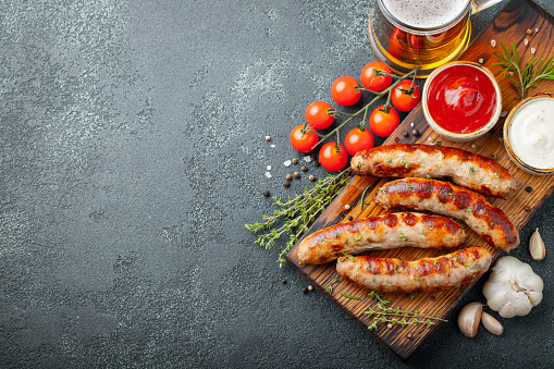 Fried sausages with sauces and herbs on a wooden serving Board. Great beer snack on a dark background. Top view with copy space.