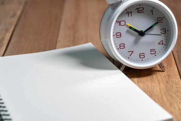 istock Empty notebook with white vintage alarm clock on the wooden table. Copy space for add text. 1051478772