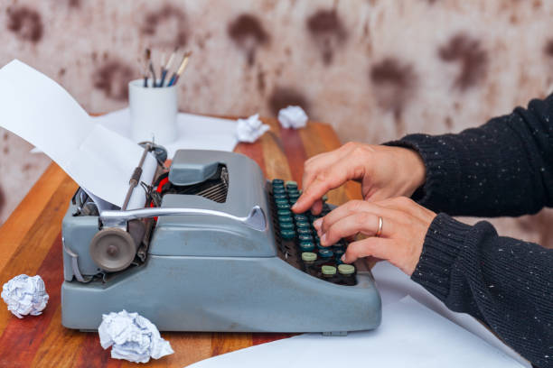 mężczyzna w swetrze wpisując na staroświeckiej maszynie do pisania. na stole są okulary i jest kubek - machine typewriter human hand typing zdjęcia i obrazy z banku zdjęć