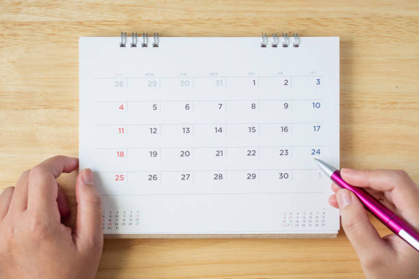 istock calendar page on table with female hand holding pen, top view 1051511650