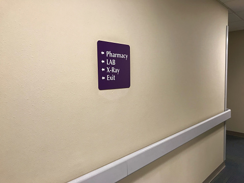 Purple directional sign on beige clinic wall above handrail in a clinic for pharmacy, Xray, lab and the exit