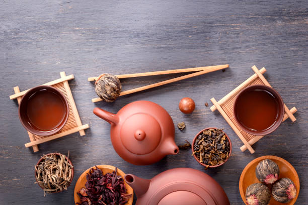 istock Several types of green tea, black tea, hibiscus tea and tea ceremony attributes - a ceramic teapot, cups, a strainer, chopsticks and tweezers are placed on an old wooden table 1051570906