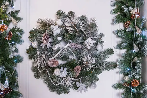 Photo of Christmas wreath with baubles, cones and evergreen boughs on a white door.Wreath decoration at door for Christmas holiday.entrance to home with holiday wreath. House decoration.