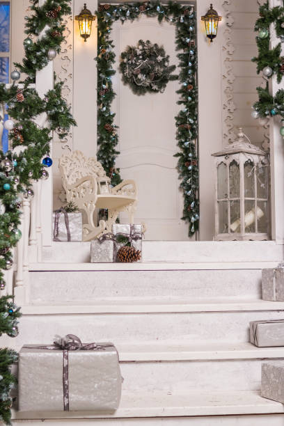de ingang van het huis ingericht voor vakantie. kerstdecoratie. garland van spar boomtakken en lichten op het railing.festively ingericht huis. lantaarn, gave boxex in zilver. vakantie briefkaart - xmas tree stockfoto's en -beelden