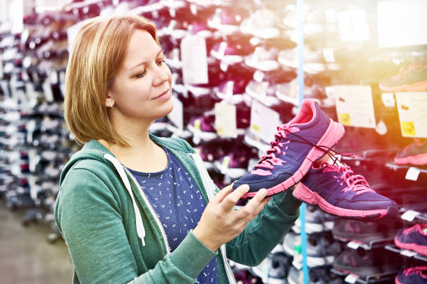 woman chooses running shoes in store - shoe store shoe shopping retail imagens e fotografias de stock